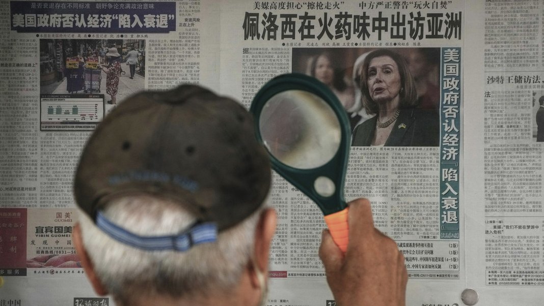 Un hombre utiliza una lupa para leer en un periódico de Beijing información sobre posible visita de Nancy Pelosi a Taiwán.