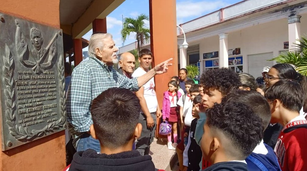 El historiador de la ciudad de Ciego de Ávila, Ángel Cabrera Sánchez, junto jóvenes ante la tarja que señala el lugar donde resultó herido el revolucionario Raúl Cervantes.