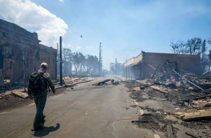 Hombre pasa junto a restos de un incendio forestal en Lahaina